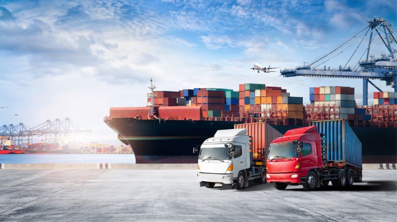 twee vrachtwagens op een haven met containerschippen op de achtergrond